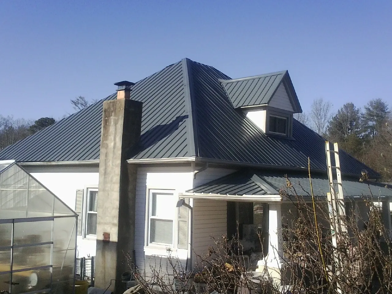 Dark blue standing seam metal roof on a white farmhouse with dormer — Slate & Tile Roof Repair by Roofing Brothers in Ava