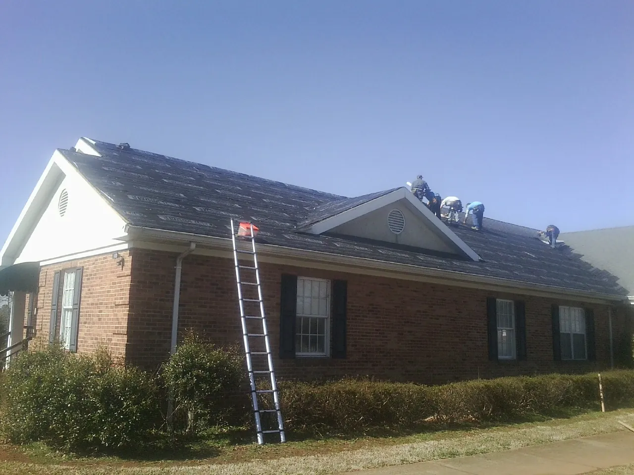 Crew tearing shingles off a brick ranch roof with a ladder set — Emergency Roof Repair work by our crew in Ava