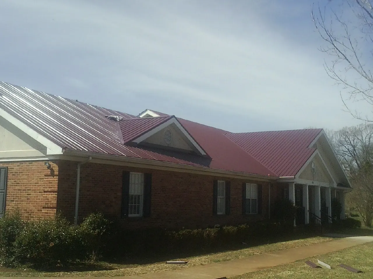 Red metal roof with gabled entries on a long brick building, from a Hail Damage Roof Repair job in Ava